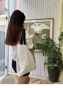 Detail of white quilted tote bag with square pattern and wide black shoulder strap