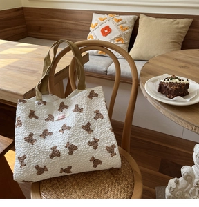 Detail of white textured fabric shoulder bag with bear print and green strap on a chair