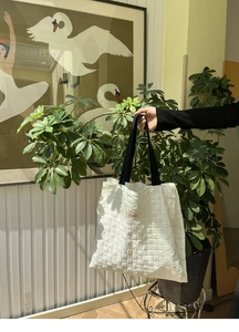 Close-up of white quilted tote bag with Sonder label and black shoulder strap texture