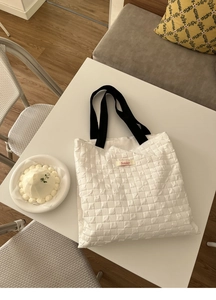 Detail of white quilted bubble tote bag featuring Sonder woven label and black strap