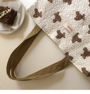 Close-up of quilted teddy bear tote bag with Sonder label next to chocolate cake