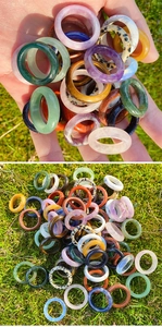 Close-up of multi-colored natural stone rings displayed on a green grass background