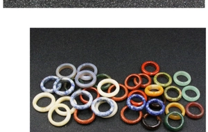 Polished natural stone rings in various colors stacked on a matte black background