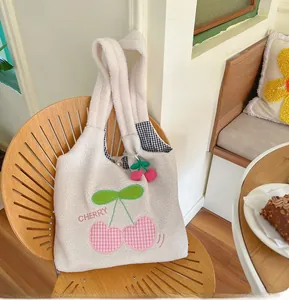 Detail of white fleece tote bag with cherry embroidery on a cozy wooden chair