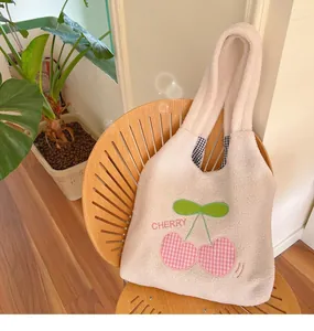 Detail of plush cream lamb wool tote bag featuring embroidered pink checkered cherries