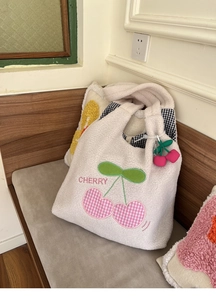 Detailed view of white fleece tote bag with pink cherry embroidery and plush charm