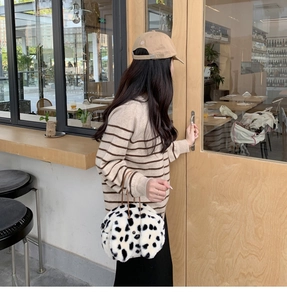 Close-up of fluffy cow print plush handbag with brown handles in a cozy cafe setting