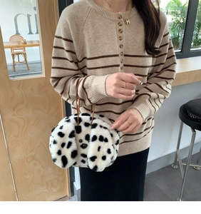 Detail of dalmatian print plush handbag with soft faux fur and brown strap on a beige sweater