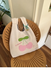 Detail of plush lamb wool tote with cherry embroidery and black check lining on a chair
