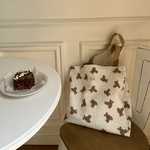 Quilted white tote bag with bear pattern and shoulder strap in a cafe setting