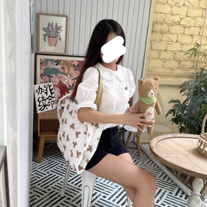 Minimalist white tote bag with bear print and brown straps shown in a cozy indoor setting