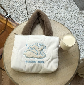 Detailed close-up of a white quilted handbag featuring sheep embroidery and brown fur handles