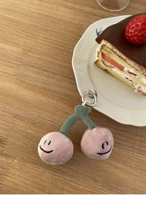 Detail eines Plüsch-Kirsch-Schlüsselanhängers mit Smiley-Stickerei auf Holztisch