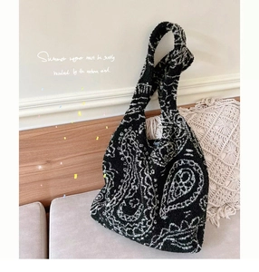 Detail of plush black and white paisley pattern handbag resting on a grey sofa