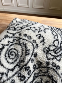 Close-up of white sherpa fabric featuring black paisley and star patterns on a tote bag