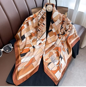 Detail of geometric floral silk scarf draped over a leather bag with premium satin finish