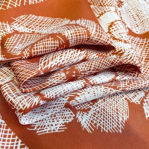 Macro shot of rust orange silk scarf featuring detailed twill weave and geometric patterns