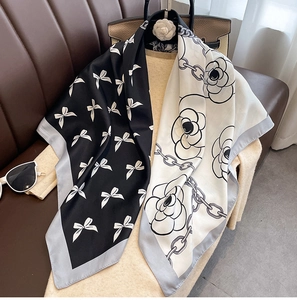 Détail d'un foulard en soie avec motifs camélia et nœuds sur un pull en maille