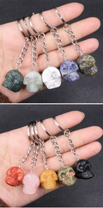 Detailed view of ten colorful crystal skull keychains held by hand for scale comparison