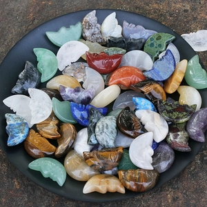 Carved natural crystal crescent moon stones with faces displayed in a black tray