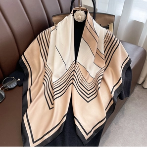 Close-up of geometric pattern silk scarf draped on a textured dark leather sofa