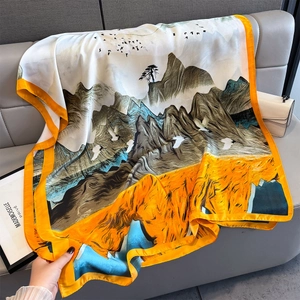 Luxurious landscape print silk scarf with vibrant orange border on leather background