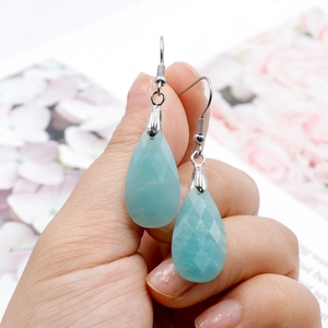 Detail of faceted Amazonite drop earrings with silver hooks held against a magazine