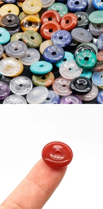 Macro detail of a colorful 12mm natural gemstone donut bead held on a fingertip