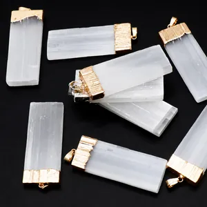 Dettaglio di ciondoli in selenite grezza con cappucci placcati in oro su superficie testurizzata