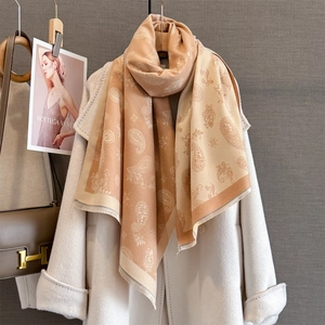 Ethnic paisley jacquard scarf in beige with tassels draped over a white coat
