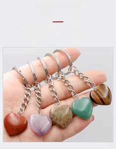 Hand holding various heart-shaped natural crystal keychains including amethyst and tiger eye
