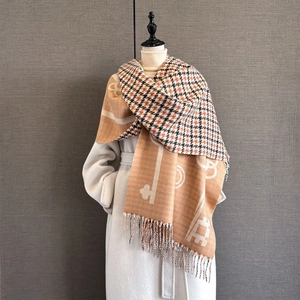 Detail of soft cashmere-like scarf showing orange and beige key patterns and thick fringe