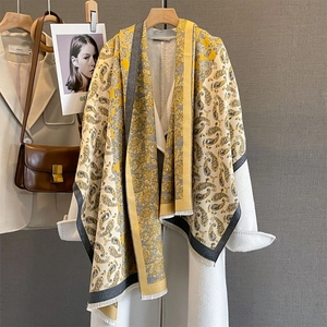 Écharpe cachemire à motif paisley jaune et gris avec franges sur un manteau blanc