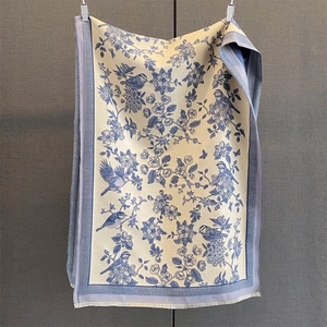 Close-up of floral and bird print scarf with soft beige fabric and blue tassel fringe