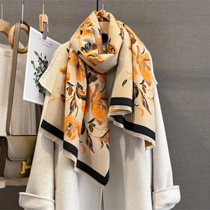 Détail de l'écharpe beige avec motifs floraux orange et finitions de bords à franges