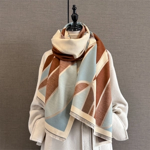 Thick geometric print scarf with tassels in caramel and blue tones on a white coat