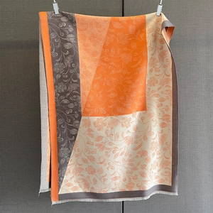 Close-up of thick scarf with geometric floral patterns, tassels, and orange-grey tones