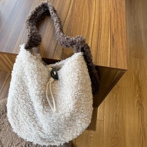 Detail of cream plush bag featuring a dark brown adjustable strap and drawstring toggle
