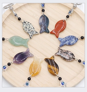 Colorful fish-shaped natural crystal pendants with Evil Eye charms on wood tray