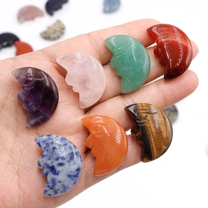 Hand holding assorted natural crystal crescent moon pendants with carved face details