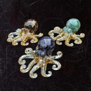 Three crystal octopus figurines with amethyst and gold leaf resin on a textured surface