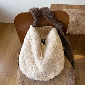 Detail of cream plush dumpling bag with dark brown strap on a wooden chair