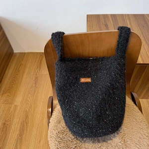 Detail view of the black plush bucket bag with white dots and brown leather logo tag