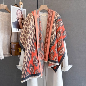 Handmade paisley print scarf with orange and grey tones draped on a white coat