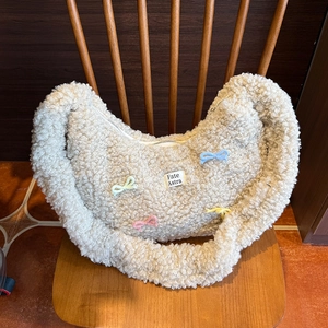 Gros plan du sac en peluche crème avec des nœuds tissés colorés posé sur une chaise en bois
