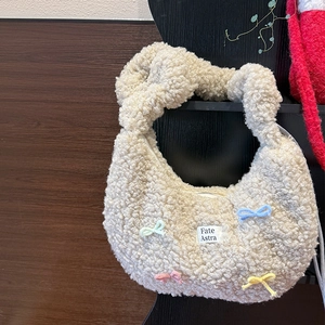 Sac hobo en peluche beige avec nœuds pastel et poignée nouée dans un décor chaleureux