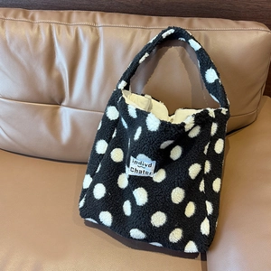 Dettaglio della borsa tote in peluche a pois bianchi e neri su un divano marrone