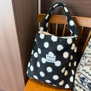 Dettaglio di una borsa tote in peluche a pois bianchi e neri su una panca di legno