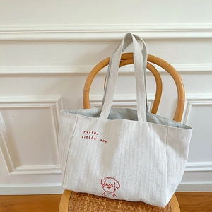 Detailed texture of beige canvas tote bag with red embroidered little dog illustration