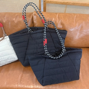 Detail of quilted cloud tote bags with striped rope handles on a leather sofa